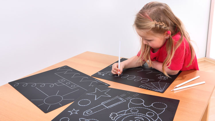 Ein Kind malt mit weißen Stiften auf schwarzem Papier