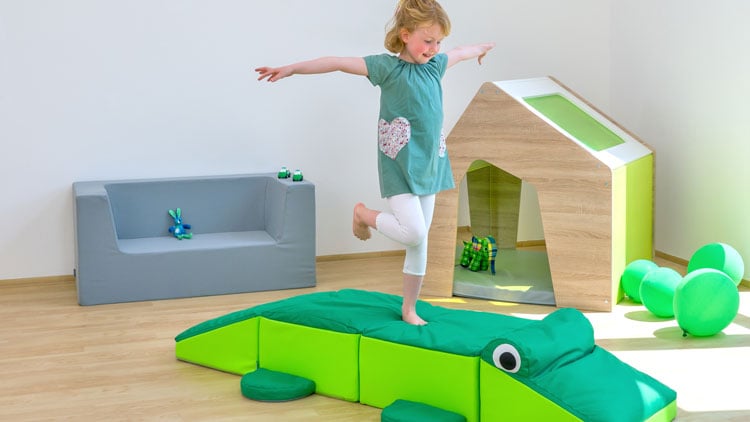 Ein Kind balanciert auf einer Matte in Krokodilform aus dem Betzold Online-Shop.