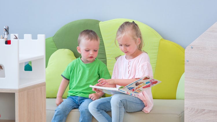 Kinder sitzen auf einem Sofa aus dem Betzold Online-Shop und lesen ein Buch.