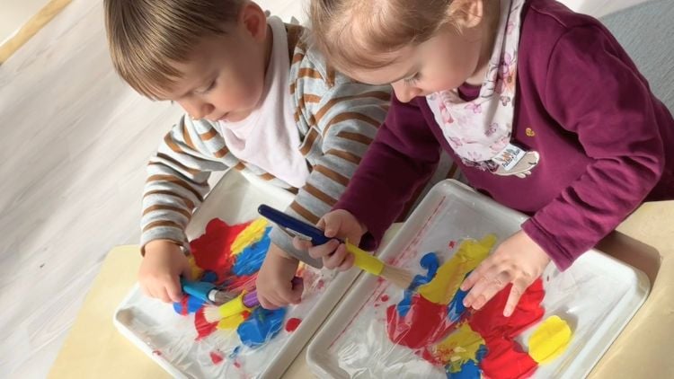 Kinder mischen Farbe in einem Plastikbeutel auf einem Aktionstablett