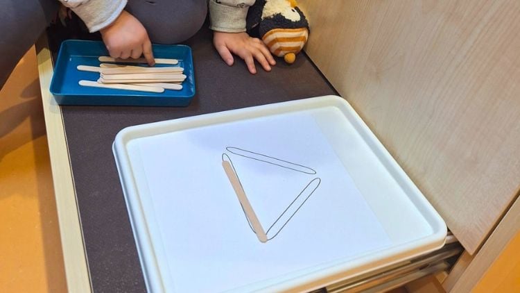 Ein Kind legt Holzstäbchen auf einer Vorlage in geometrischen Formen aus