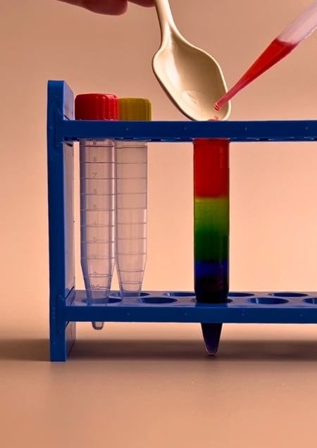 Eingefärbtes Zuckerwasser, das in unterschiedlichen Schichten in ein Reagenzglas gefüllt wird.