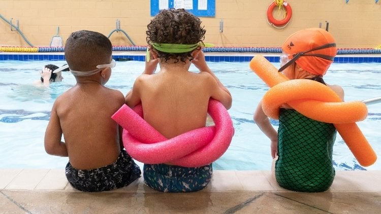 Kinder sitzen am Beckenrand eines Schwimmbads