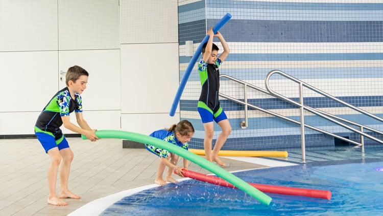Kinder spielen im Schwimmbad mit Schwimmnudeln
