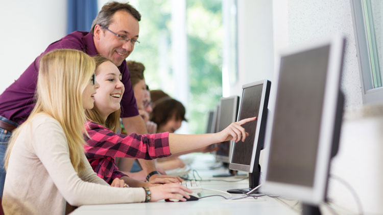 Lehrerin erklärt Schülern etwas am PC