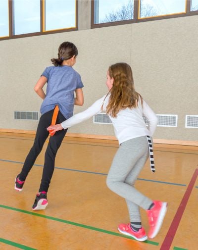 Zwei Mädchen spielen Fangen in Sporthalle