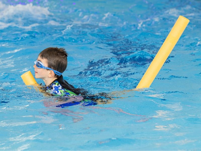 Junge schwimmt im Wasser mit Schwimmnudel