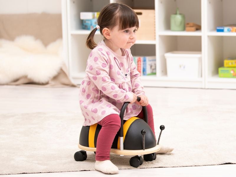 Kleinkind sitzt auf einem Rollrutscher in Form einer Biene