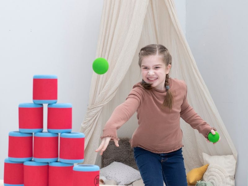 Mädchen wirft mit Ball auf gestapelte Dosen
