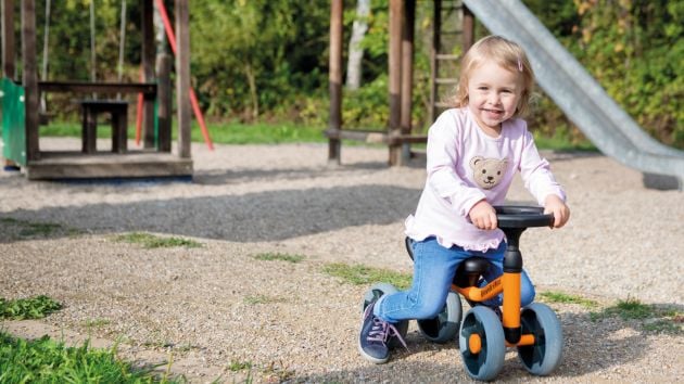 Kleinkind fährt auf Kinderfahrzeug am Spielplatz