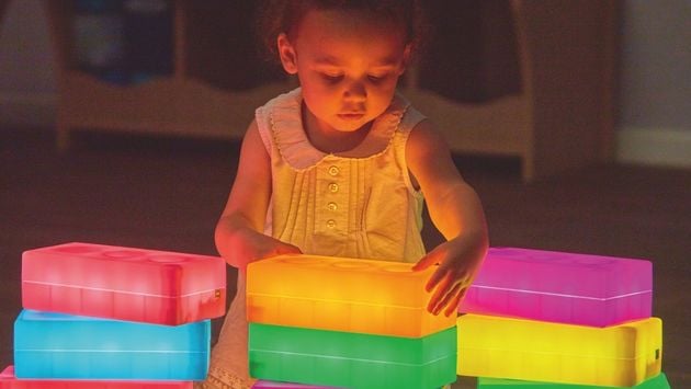 Experiment Leuchtbausteine Kleines Kind stapelt bunt leuchtende Bausteine in abgedunkeltem Raum