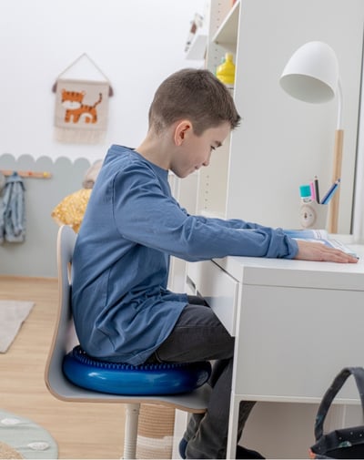 Sitzkissen Junge sitzt mit Sitzkissen auf einem Stuhl am Schreibtisch