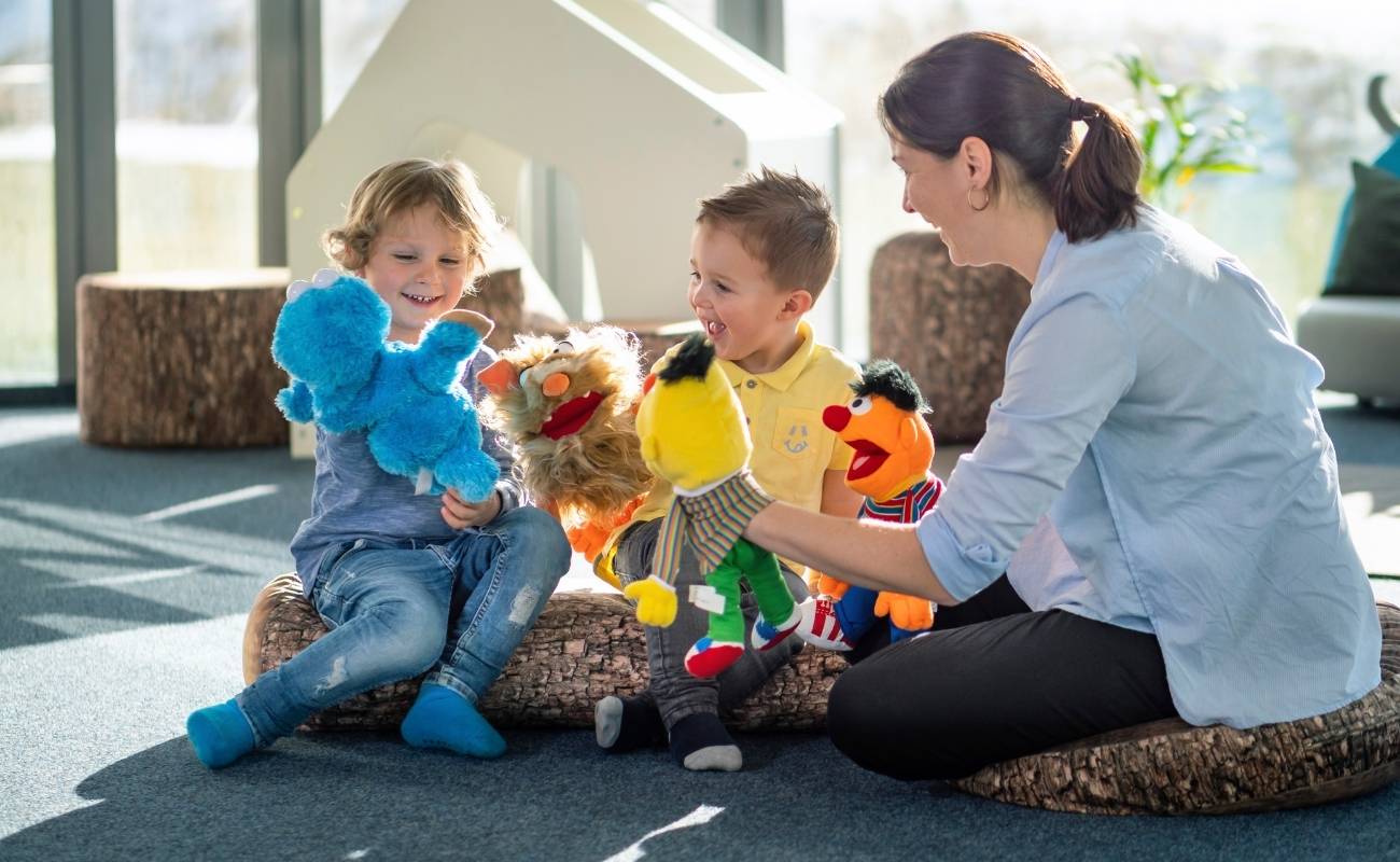 Erzieherinnen und zwei Kinder sitzen auf dem Boden und spielen mit Handpuppen