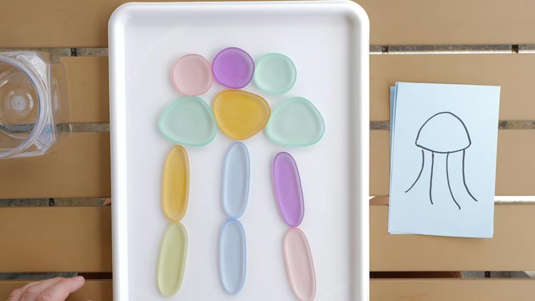 Tiere auf einem Aktionstablett mit Regenbogenkieseln aus dem Betzold Online-Shop legen.