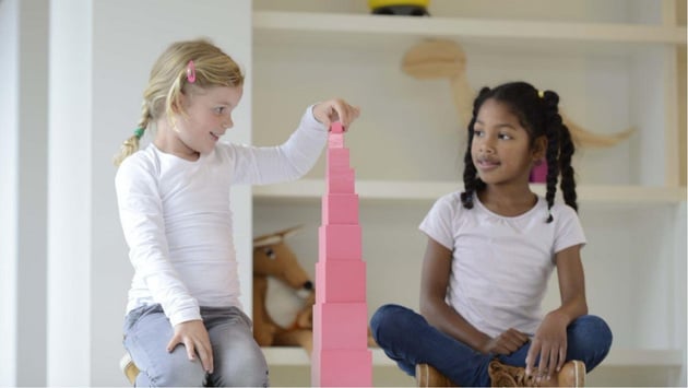 Zwei Kinder sitzen auf dem Boden und stapeln die Würfel des Rosa Turmes