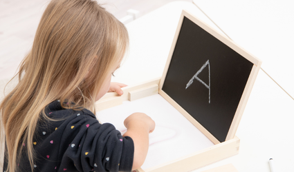 Mädchen zeichnet mit dem Finger den Buchstaben A in den Sand