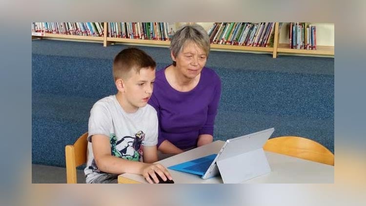 Junge und ältere Dame lesen am Laptop