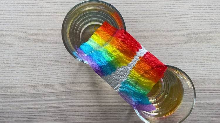 Zwei Wassergläser in denen ein auf Toilettenpapier gemalter Regenbogen "wächst"