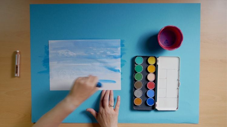 Mit weißem Wachsmaler und Wasserfarbe entstehen in Kindergarten und Kita farbenfrohe Wolkenbilder.