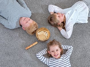 Drei Kinder liegen entspannt auf einem Teppich rund um eine Klangschale und genießen eine gemeinsame Ruhepause.