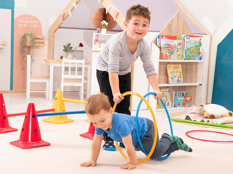 Zwei Kinder spielen mit bunten Reifen in einem Bewegungsparcours.