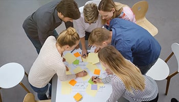 Personen stehen um einen Tisch mit Notizen und diskutieren